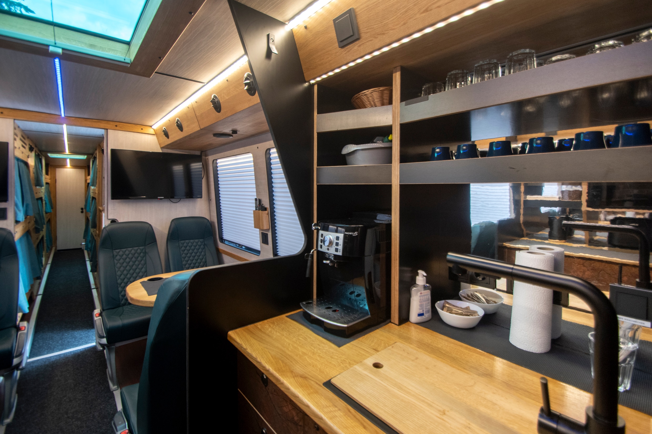 Interior of a tour bus with lounge seating, kitchenette and sleeping bunks