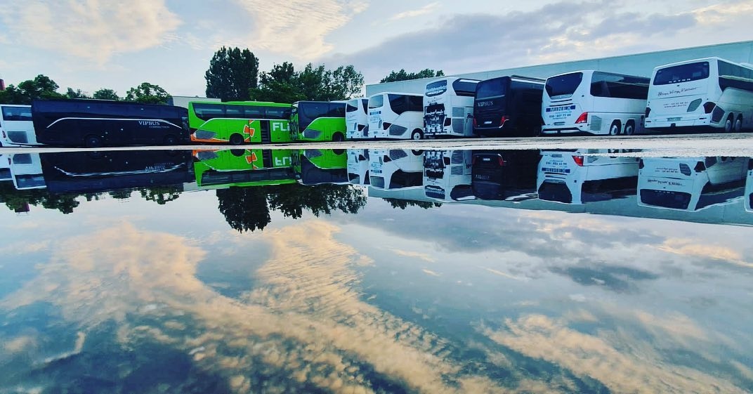 Coaches parked side by side, mirrored in a puddle under the evening sky